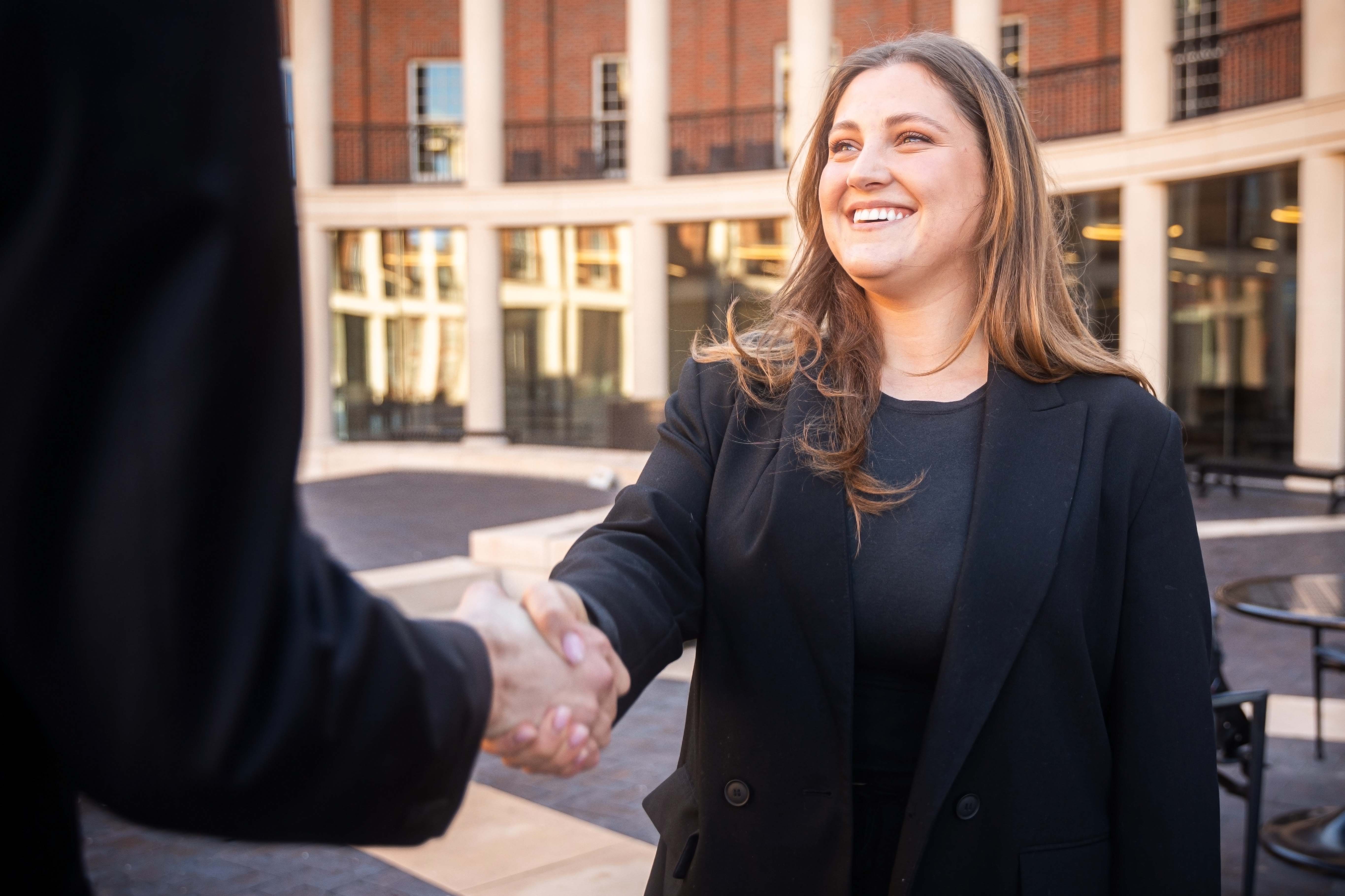 Female student smiling and shaking hands with someone.