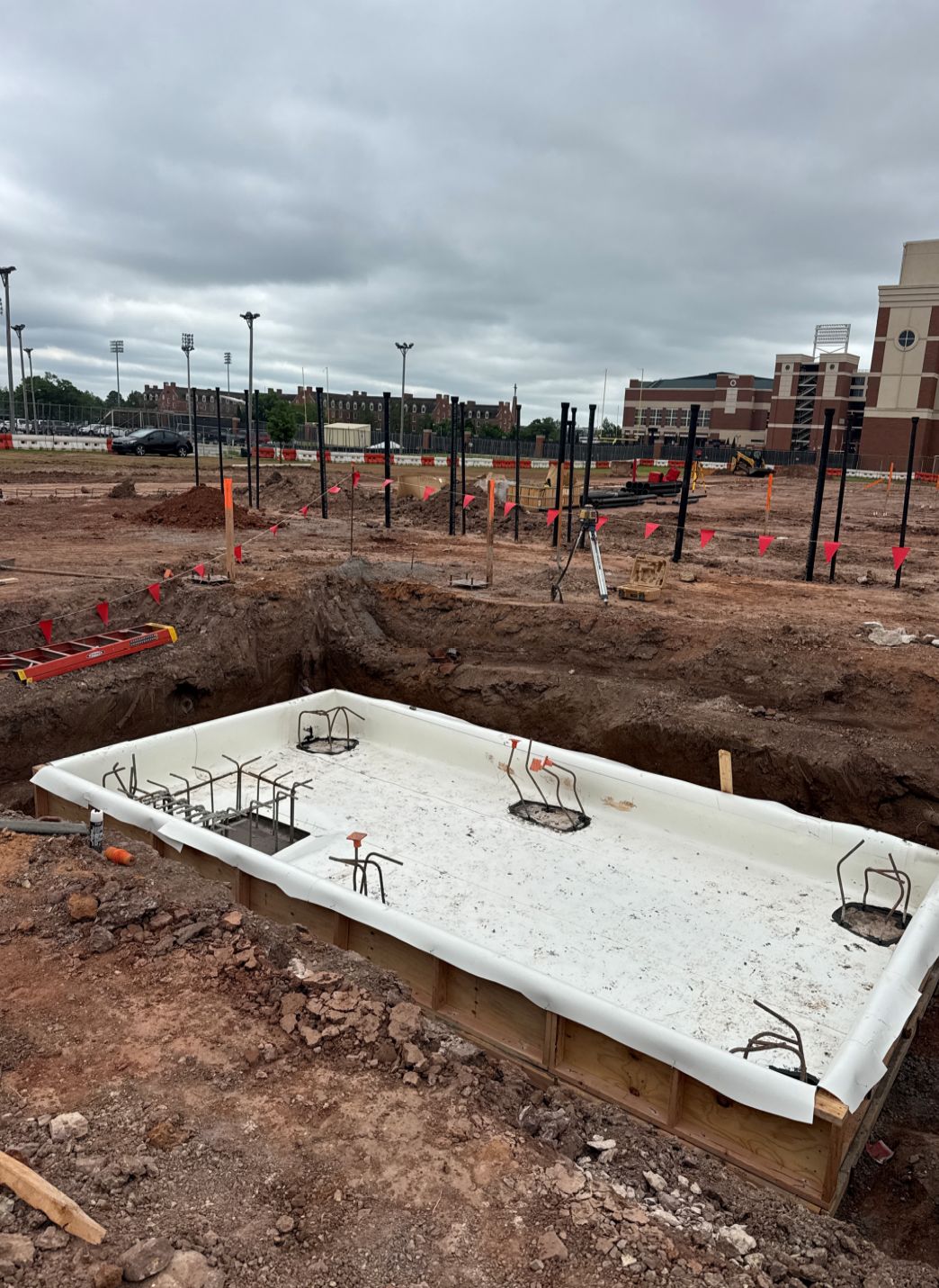 Construction site with a waterproofed elevator pit, with drainage and exposed rebar installed under cloudy skies.