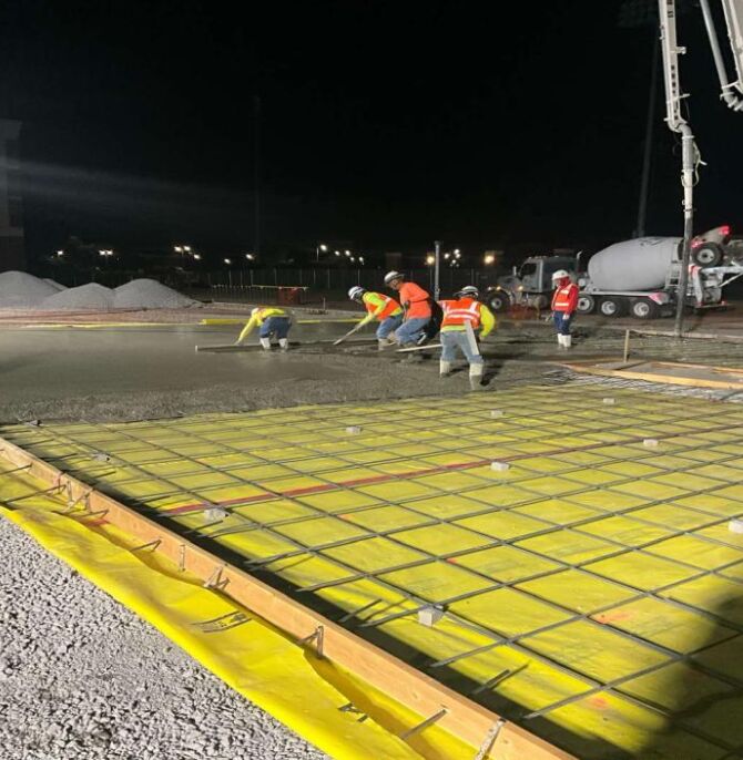 Construction workers pour and level concrete over rebar grid for building slab