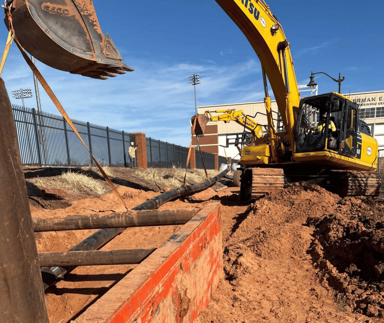 two excavators lay a black pipe in a trench
