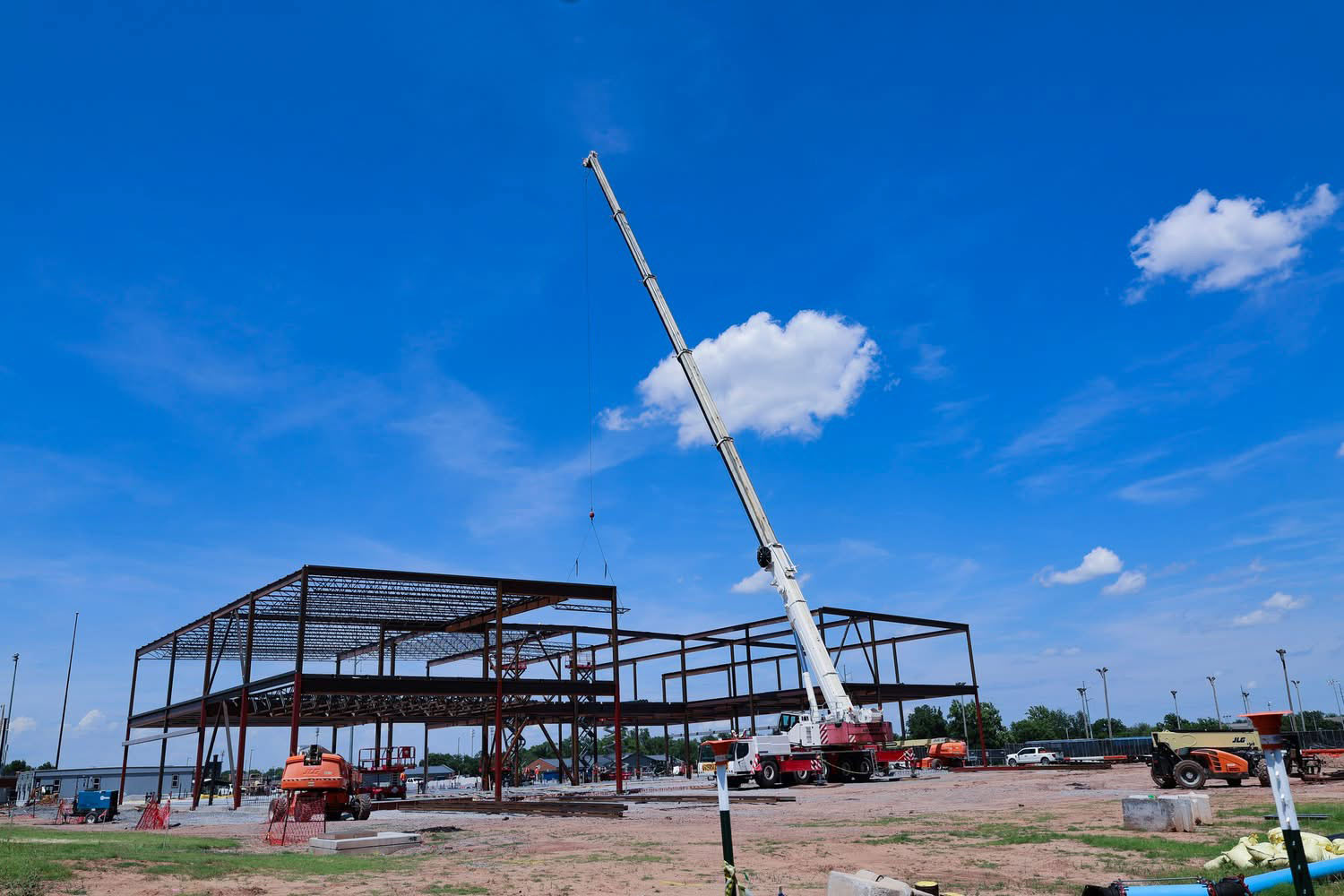 Wide view of a steel building frame under construction with a crane lifting structural beams on the job site.