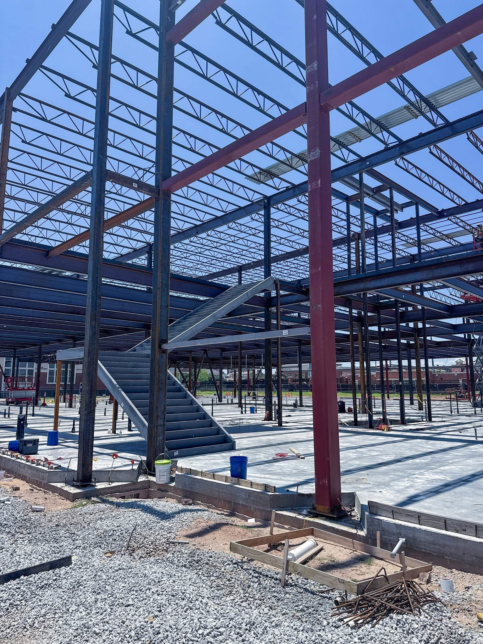 Interior view of a steel-framed building under construction with a newly installed staircase and concrete floor.
