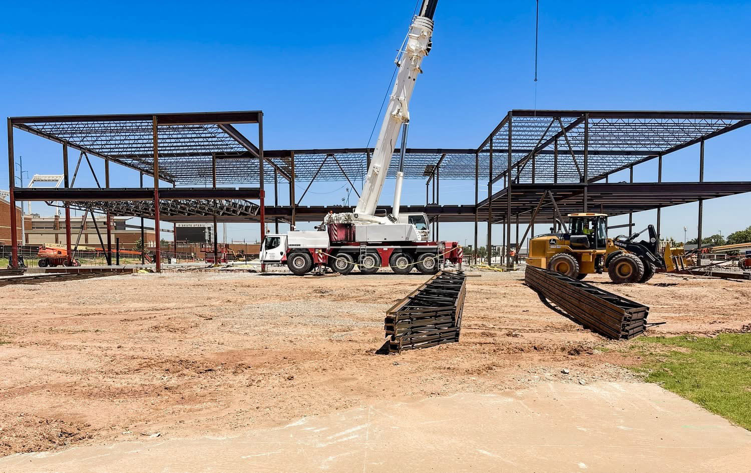 Steel framework for a new campus building under construction with a crane and heavy equipment on site.