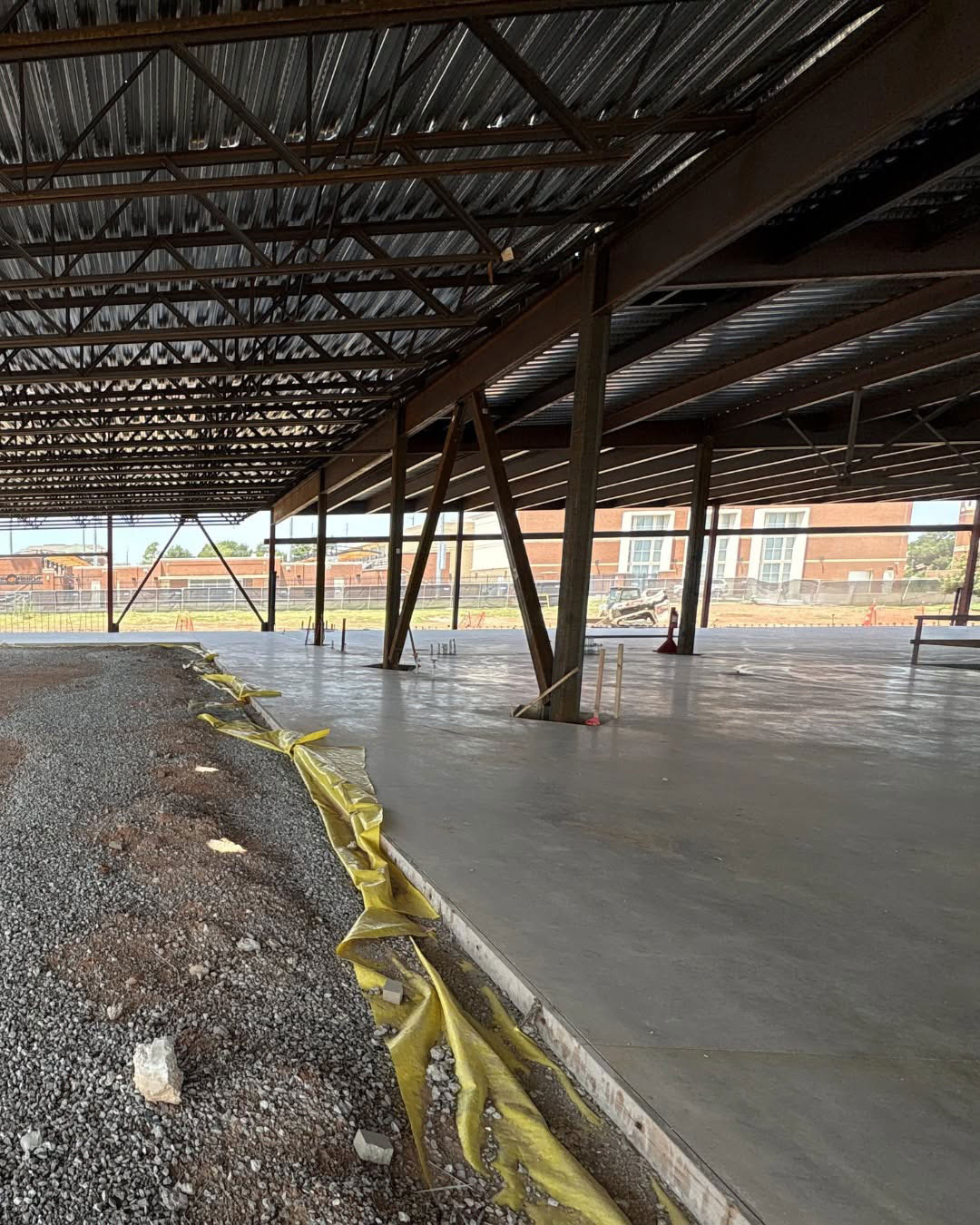 Interior view of the Boone Pickens Human Performance Innovation Complex under construction, showing steel framing, a newly poured concrete floor and metal roofing.