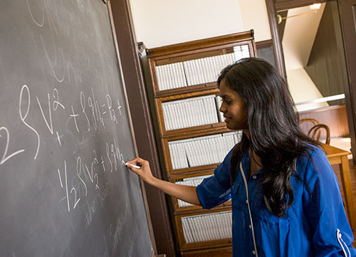 A student writes an equation on a chalkboard.