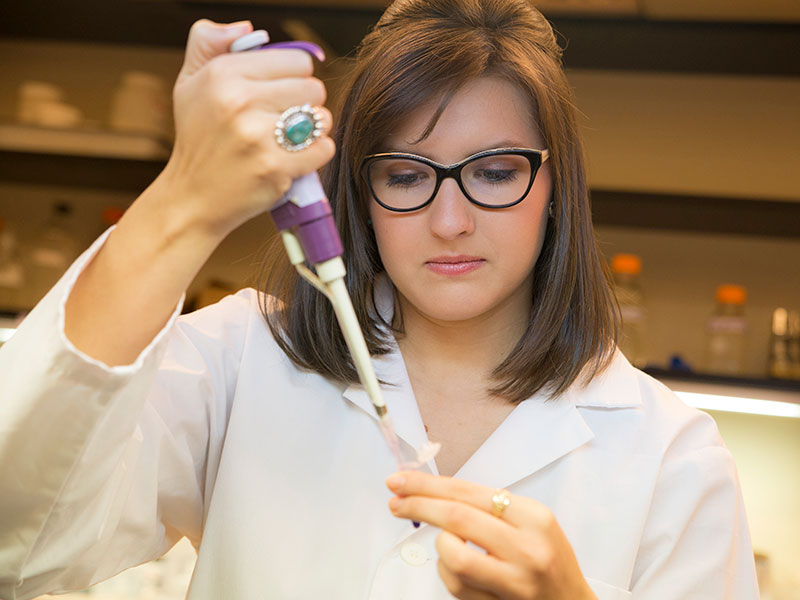 A student fills a pipette in a lab.