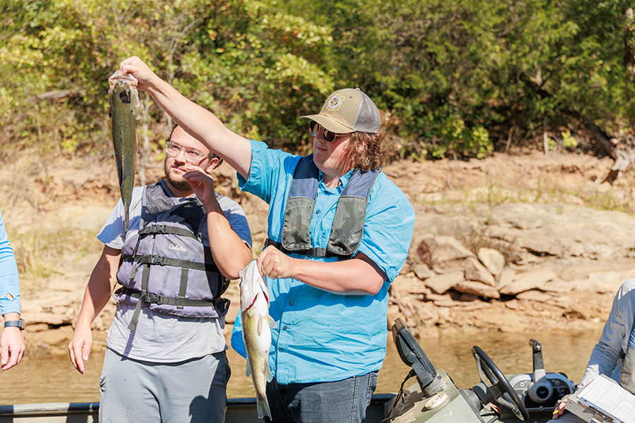Fisheries and Aquatic Ecology A student standing in a boat holding two fish while another student observes