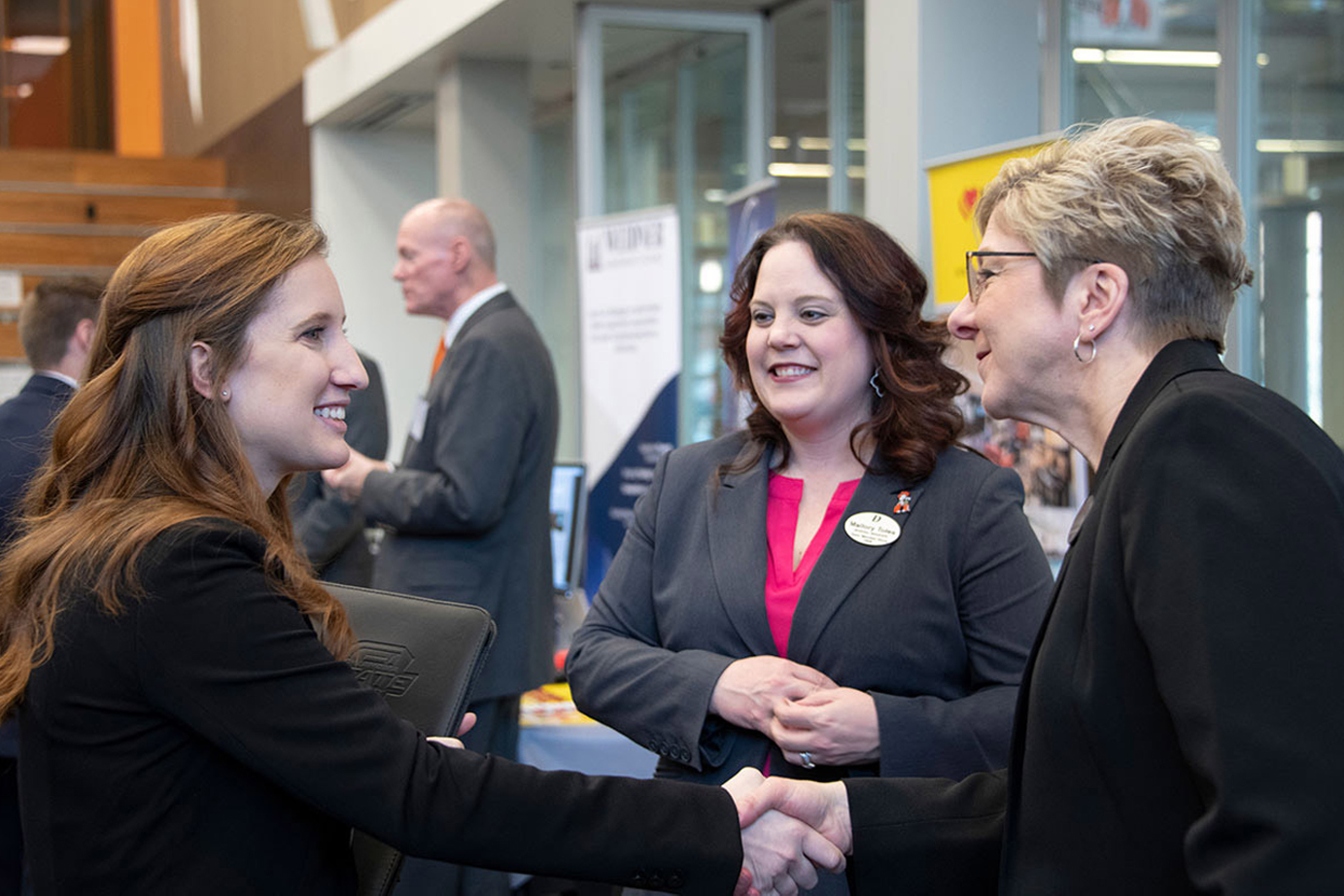 Female student dressed professionally shakes hands with a female employer.