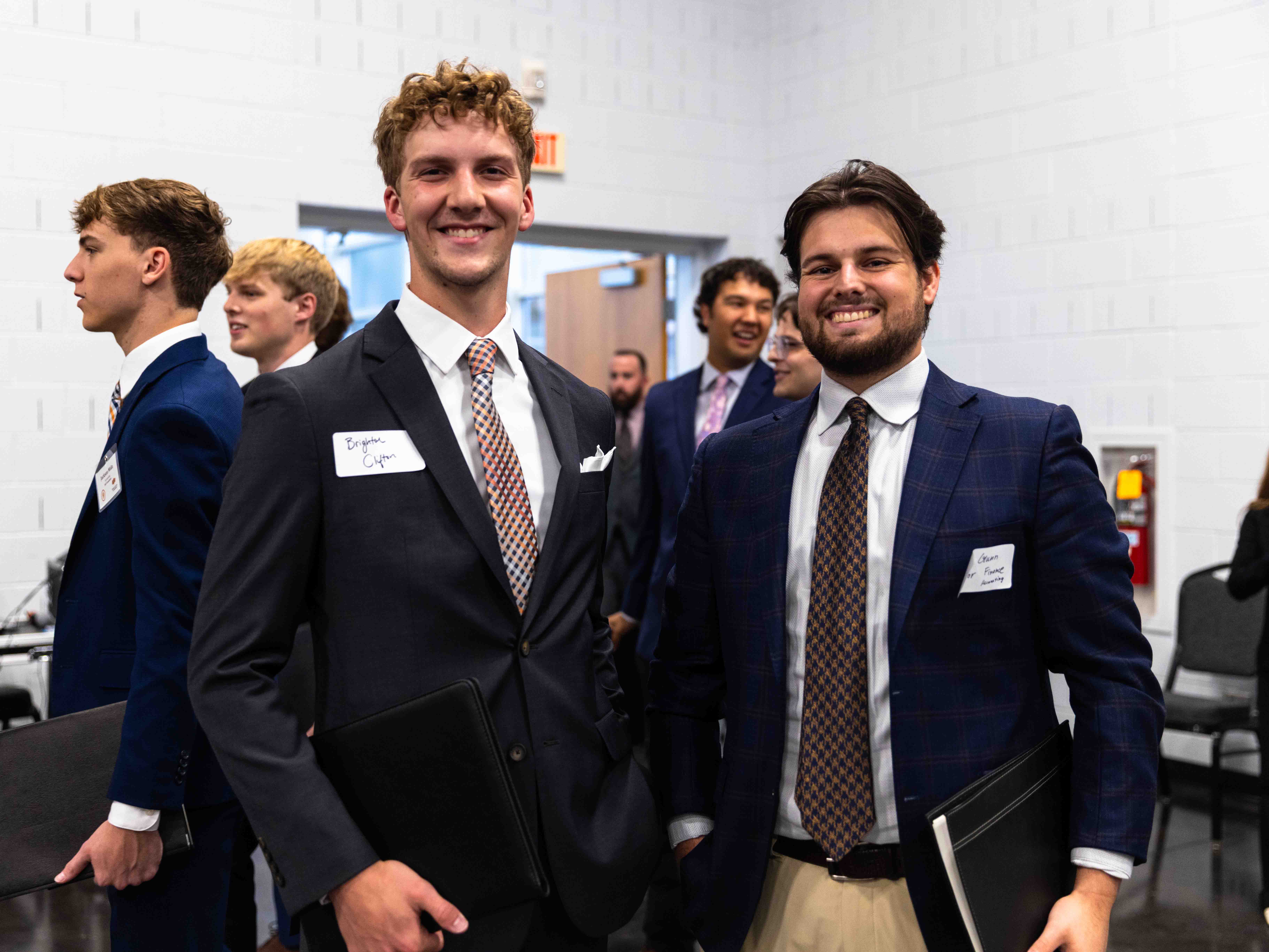 Two male students dressed in suits smile.